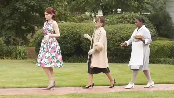 Three women cross a lawn while one carries a freshly baked pie