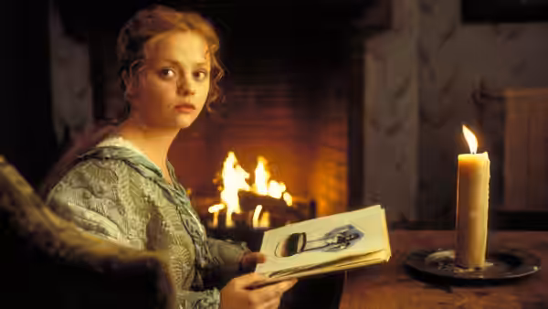 Katrina Van Tassel (Christina Ricci) studies an illustrated book beside a roaring fireplace