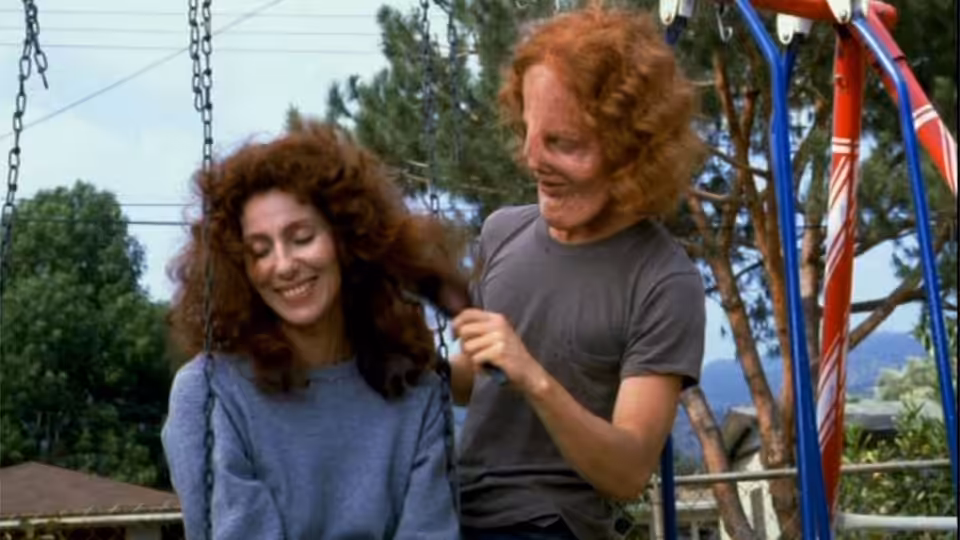 Rusty Dennis (Cher) smiles as Gar (Sam Elliott) stands beside her at a playground