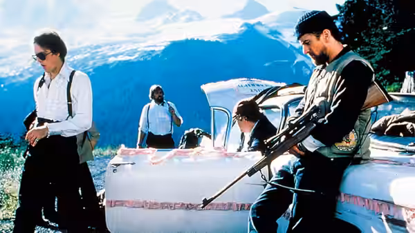 Men with a white car in mountains one holding a rifle on hood