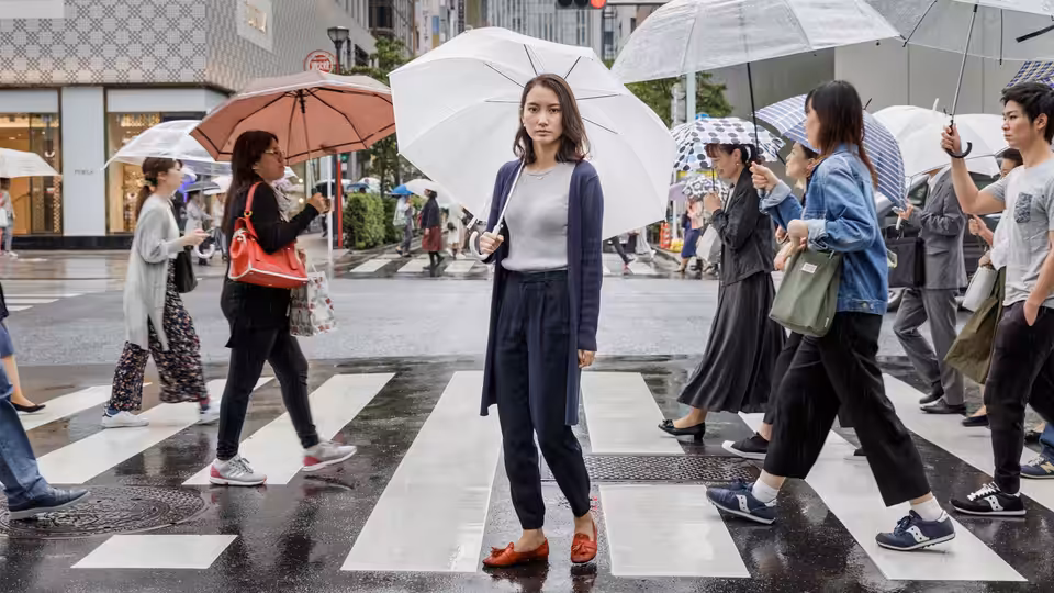 Shiori Itō stands beneath a white umbrella on a busy city crosswalk