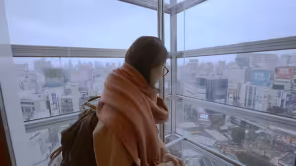 A woman in a scarf looks out over Tokyo from a high-rise window