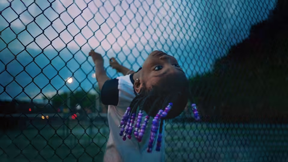A young girl reaches up to a chain-link fence outdoors