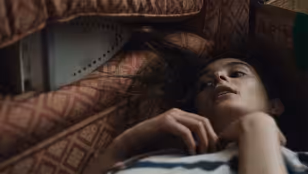 A young woman lies among patterned cushions, gazing upward