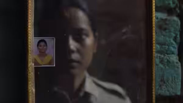 A policewoman's reflection appears in a mirror beside a small portrait
