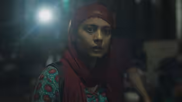 A woman in a red headscarf faces forward in a dimly lit room