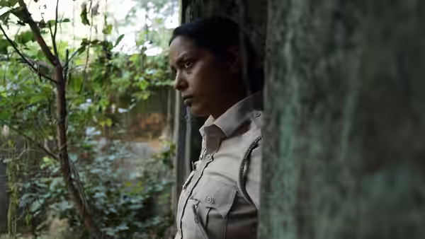 Constable Santosh Saini (Shahana Goswami) peers through foliage beside a window