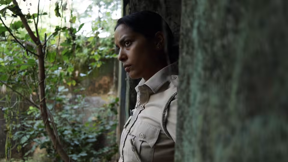 Constable Santosh Saini (Shahana Goswami) peers through foliage beside a window