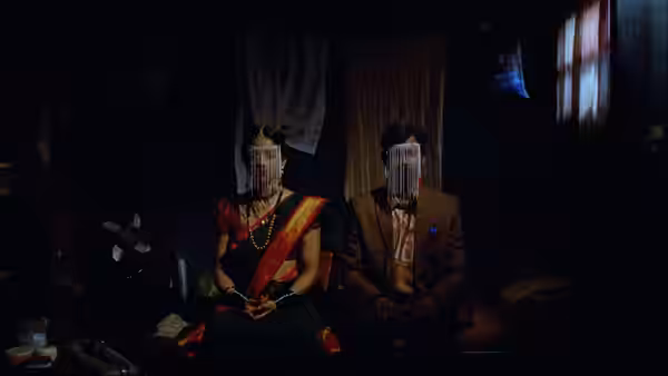 A bride and groom sit side by side in a dark room, their faces veiled