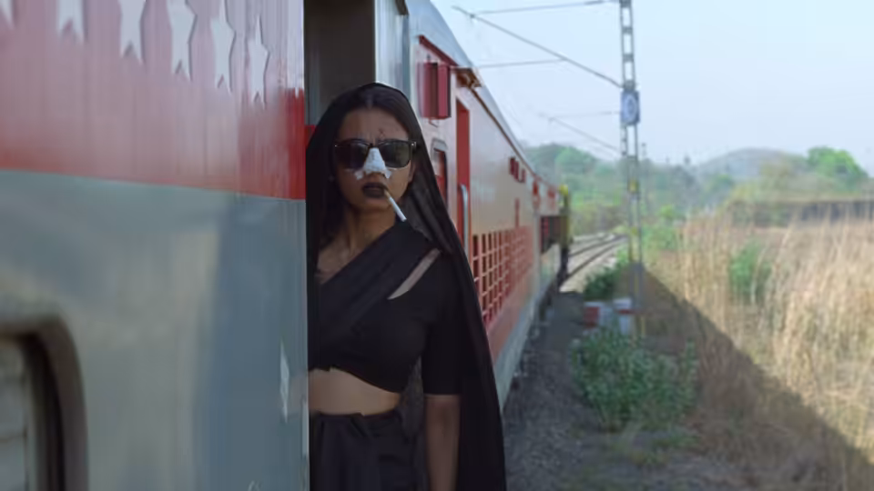 Uma (Radhika Apte) stands beside a train, wearing sunglasses and smoking