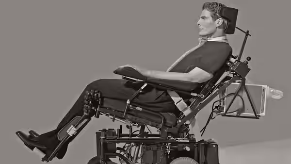 Christopher Reeve reclines in a wheelchair with head support and equipment attached