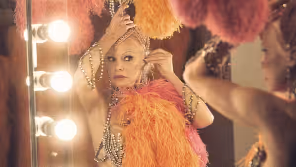 Shelly (Pamela Anderson) adjusts her feathered headdress before a lit dressing-room mirror