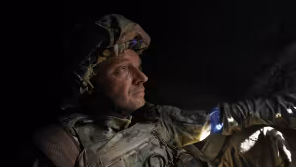 A helmeted soldier reaches forward inside a dark shelter