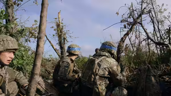 Ukrainian soldiers gather among broken trees in a forest