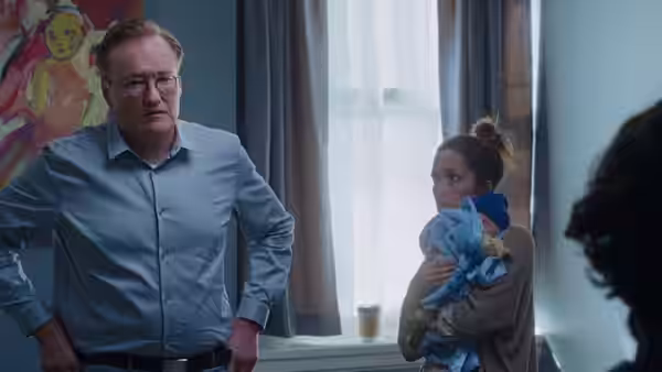 Linda holds a bundled child beside her therapist (Conan O’Brien) in a bright office