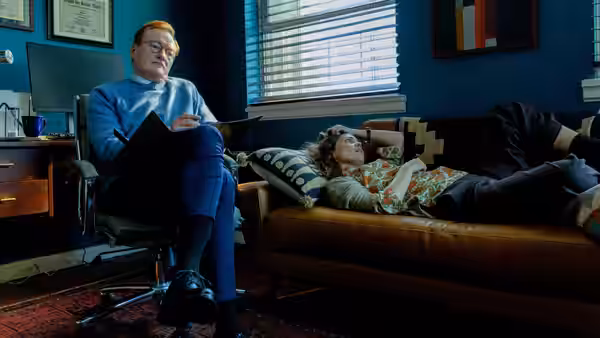 Linda (Rose Byrne) reclines on a couch while her therapist (Conan O’Brien) sits nearby with a clipboard