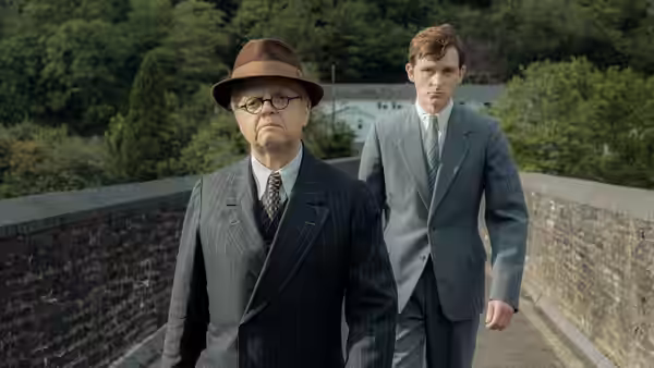 Philip Burton (Toby Jones) and Richard Jenkins Jr. (Harry Lawtey) walk along a stone bridge