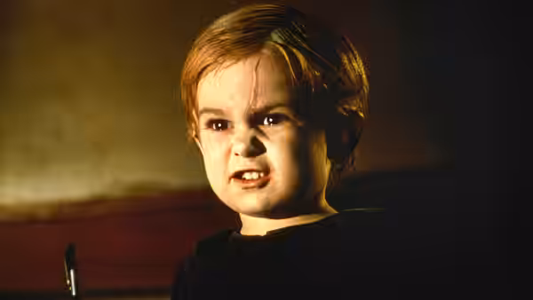 A young boy glares angrily in a dimly lit room