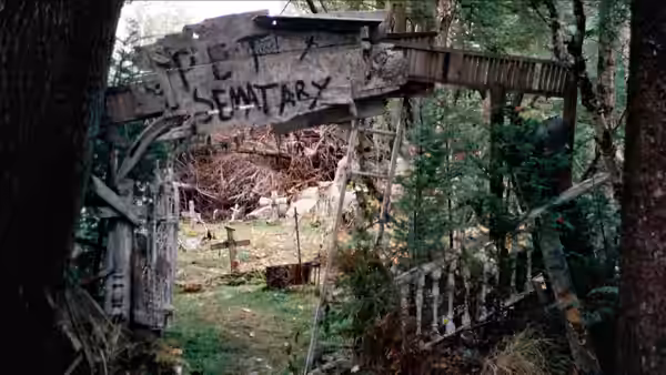 A weathered Pet Sematary sign marks a wooded path lined with small graves
