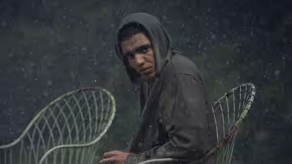 A hooded young man sits alone on a rain-soaked metal chair