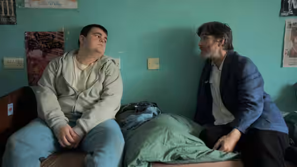Steve talks with a young man beside a bed in a residential room