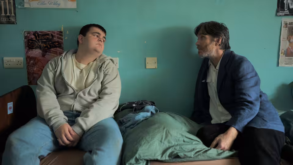 Steve talks with a young man beside a bed in a residential room