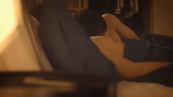 Two men lie together under a blanket in bed