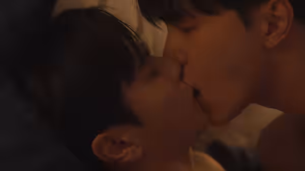 Two men kiss while lying close together in bed
