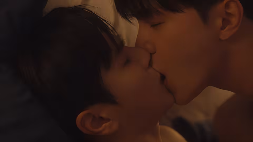 Two men kiss while lying close together in bed
