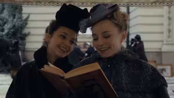 Two women in hats smile together while reading an open book outdoors