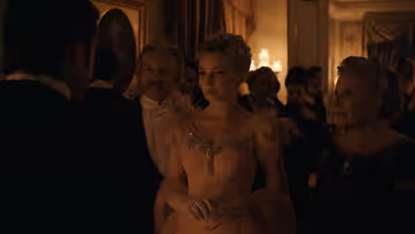A young woman in an evening gown stands among guests at a candlelit ballroom