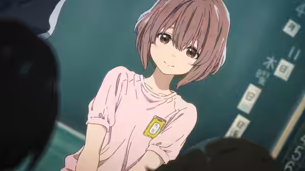 A girl with short pink hair sits in a classroom wearing a pink shirt with a name tag