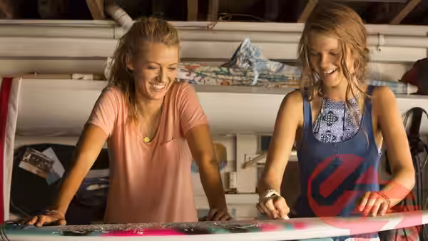 Two young women smile as they examine a surfboard inside a shop