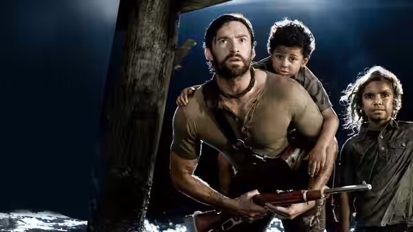 The Drover (Hugh Jackman) holds a rifle as two boys shelter close beside him at night
