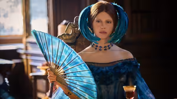 Elizabeth (Mia Goth) holding a blue fan in period attire