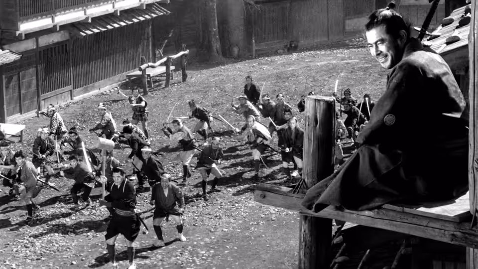 Samurai smiles from a wooden platform above many swordsmen clashing in a courtyard