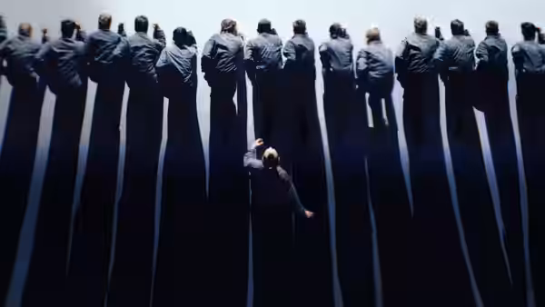 A man reaches toward a line of dancers standing above him against a dark backdrop