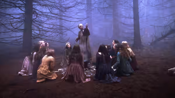 A group of young women gather around a standing figure in a misty forest