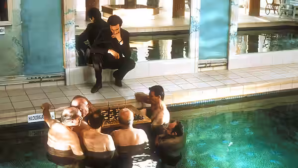 A man sits beside an indoor pool as several men gather in the water