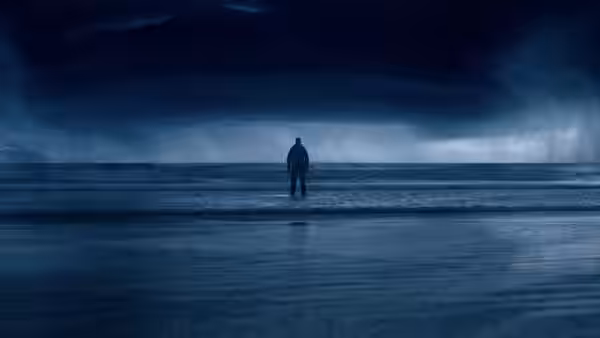 A lone figure stands on a beach beneath heavy storm clouds