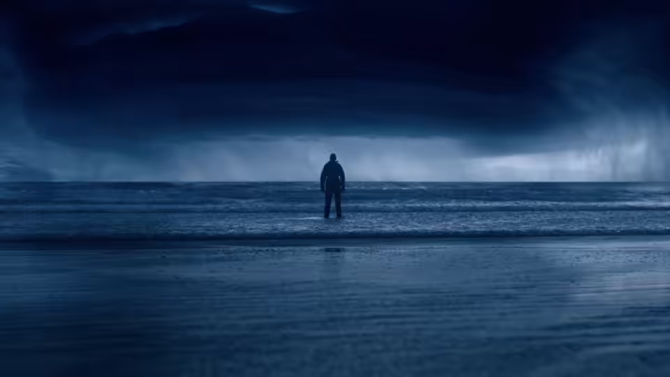 A lone figure stands on a beach beneath heavy storm clouds