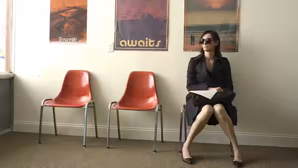 Eva (Tilda Swinton) sitting alone in a waiting area with red chairs