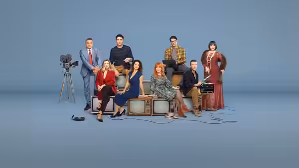 Seven people pose around vintage televisions and a film camera against a blue studio backdrop