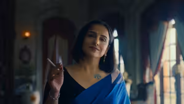 A woman in a blue sari holds a cigarette inside an ornate room