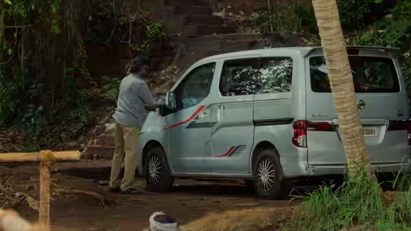 A man stands beside a parked van on a wooded path