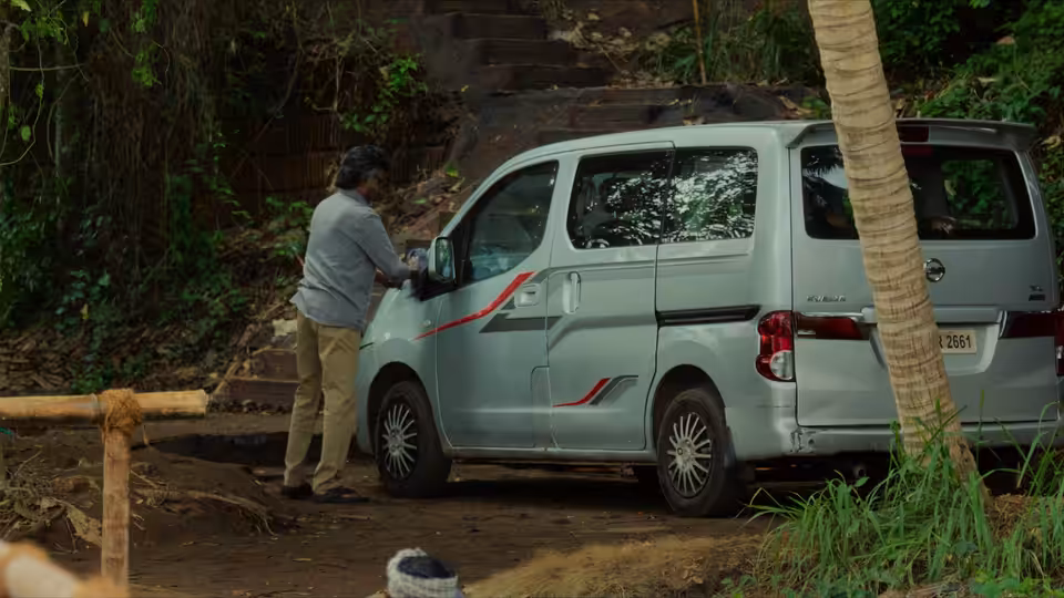 A man stands beside a parked van on a wooded path