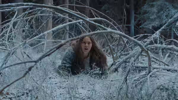 Saga (Seidi Haarla) crawls through snow-covered branches in a forest