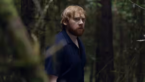 Jon (Rupert Grint) stands among trees, looking warily to one side