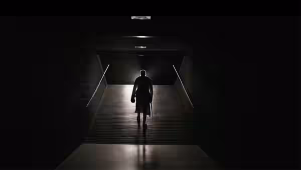 A silhouetted figure walks up a dark passage toward a lit arena entrance