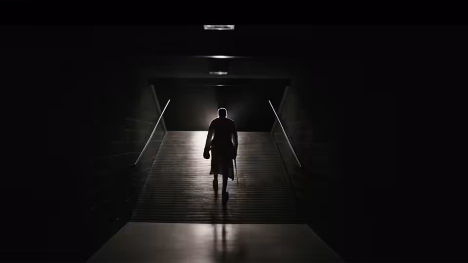 A silhouetted figure walks up a dark passage toward a lit arena entrance